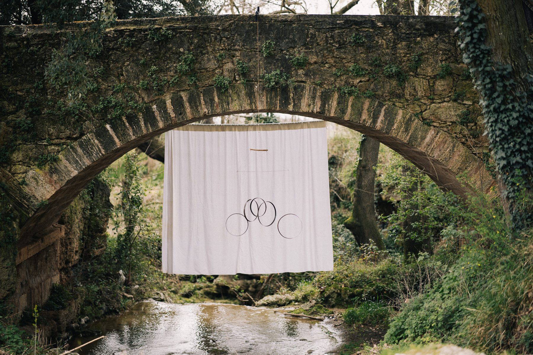 Wine cask hoops mobile hanging under a stone bridge over a stream
